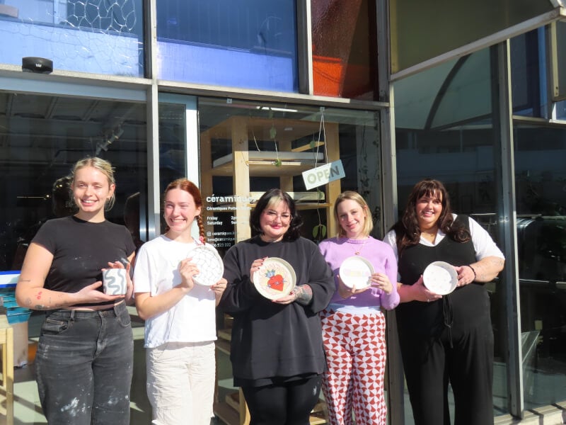 Team standing and holding up plates in front of a ceramics studio